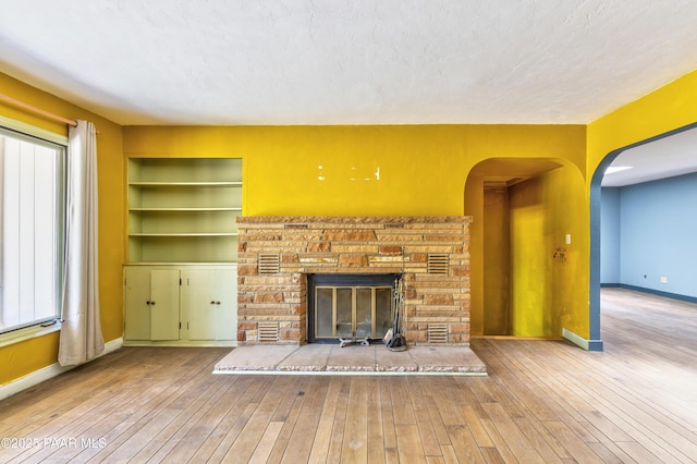 769 Cherokee Rd, Prescott, AZ 86303 - unfurnished living room with a glass covered fireplace, hardwood / wood-style flooring, a textured ceiling, arched walkways, and built in shelves