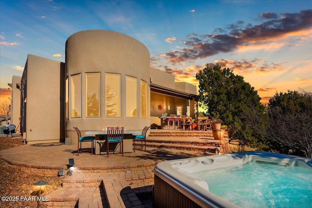 pool at dusk with a patio area and a hot tub