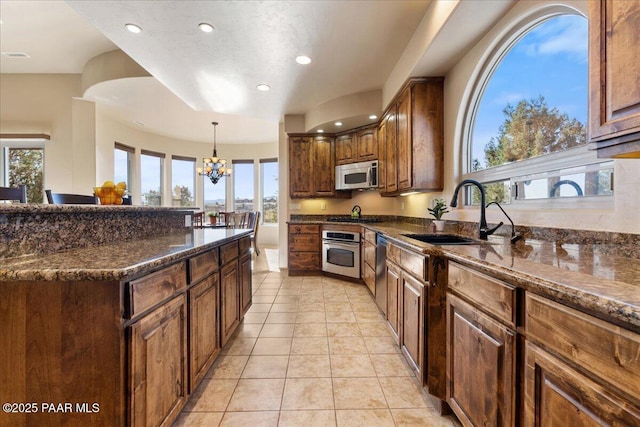 kitchen featuring sink, dark stone counters, a chandelier, light tile patterned floors, and appliances with stainless steel finishes