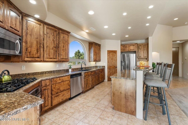 kitchen with sink, stainless steel appliances, dark stone counters, a breakfast bar area, and a kitchen island