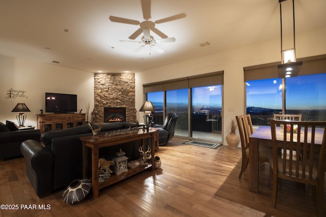 living room featuring hardwood / wood-style flooring, a stone fireplace, and ceiling fan