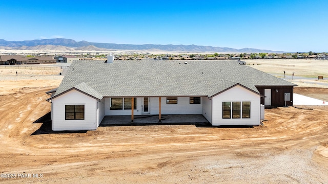 view of front of house featuring a patio, a chimney, a shingled roof, and a mountain view