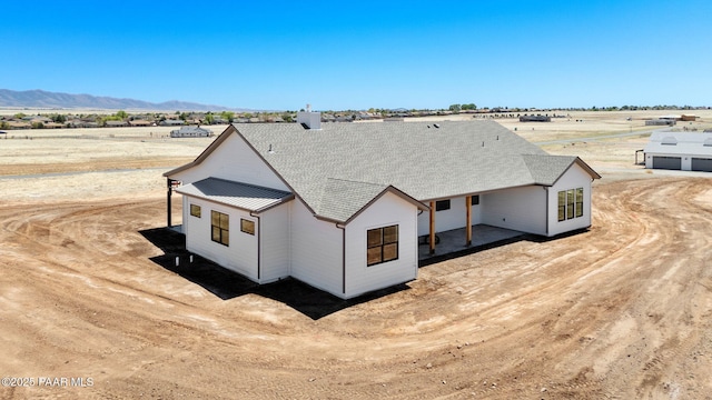 back of property with a mountain view, a rural view, and roof with shingles