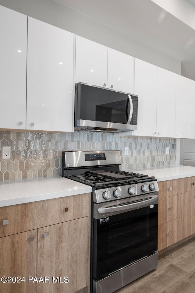 kitchen with backsplash, light hardwood / wood-style flooring, white cabinets, and stainless steel appliances