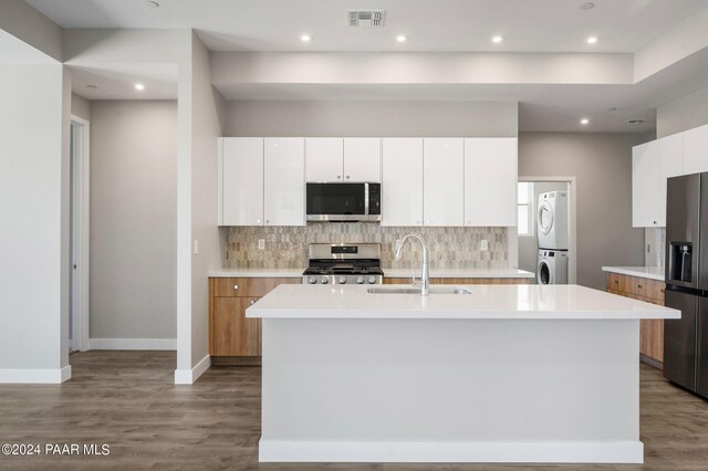 kitchen featuring a center island with sink, stacked washer and dryer, sink, appliances with stainless steel finishes, and white cabinetry