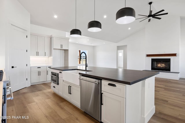 kitchen featuring hanging light fixtures, stainless steel appliances, white cabinets, and a center island with sink