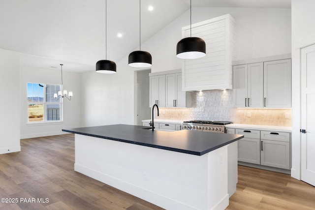 kitchen featuring pendant lighting, a kitchen island with sink, sink, and stove