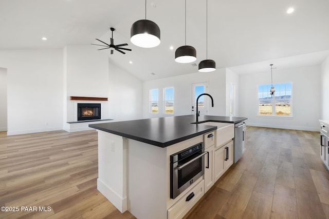 kitchen featuring pendant lighting, sink, appliances with stainless steel finishes, white cabinets, and a center island with sink