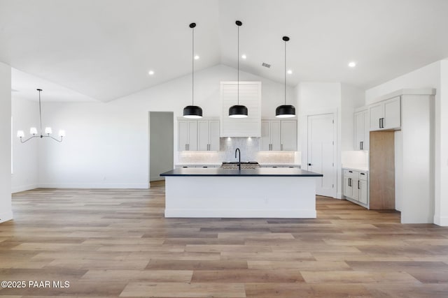 kitchen with light hardwood / wood-style flooring, hanging light fixtures, high vaulted ceiling, tasteful backsplash, and a center island with sink