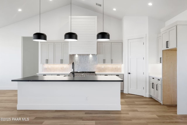 kitchen featuring pendant lighting, high vaulted ceiling, a kitchen island with sink, and light wood-type flooring