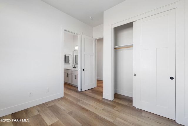 unfurnished bedroom featuring sink, connected bathroom, light hardwood / wood-style floors, and a closet