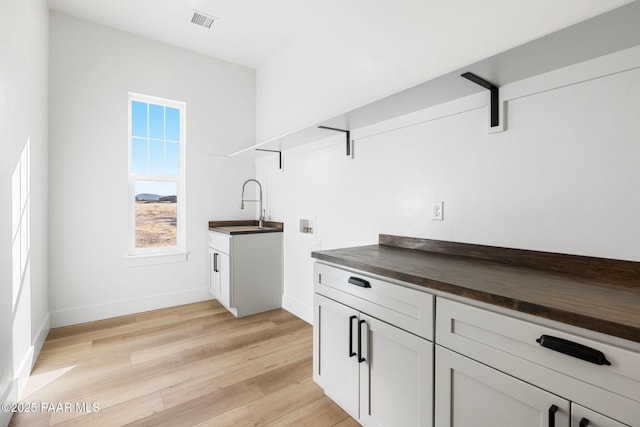 kitchen with butcher block counters, sink, white cabinetry, and light hardwood / wood-style flooring