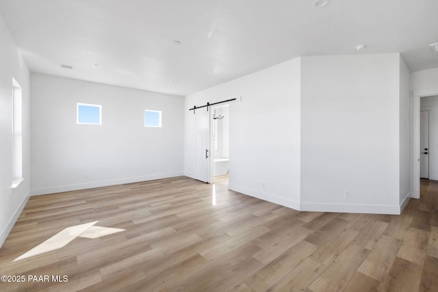 spare room with a barn door and light hardwood / wood-style floors