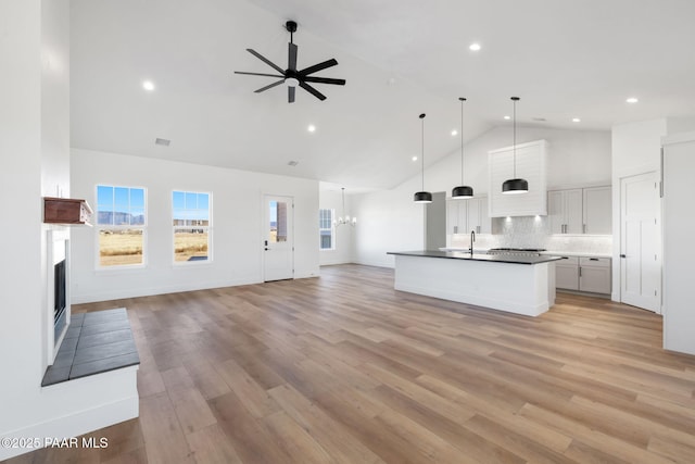 kitchen with light hardwood / wood-style flooring, ceiling fan with notable chandelier, a kitchen island with sink, high vaulted ceiling, and decorative light fixtures