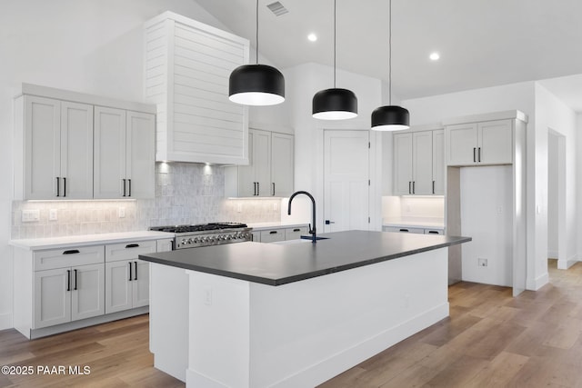 kitchen featuring sink, hanging light fixtures, range, a center island with sink, and light hardwood / wood-style flooring