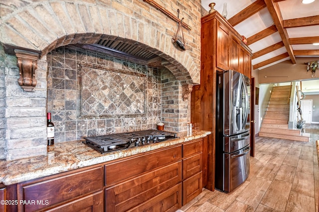 kitchen featuring stainless steel refrigerator with ice dispenser, vaulted ceiling with beams, tasteful backsplash, light stone counters, and gas cooktop