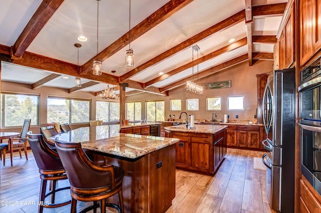 kitchen with hanging light fixtures, stainless steel appliances, light stone counters, a notable chandelier, and an island with sink