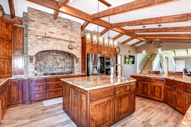 kitchen with pendant lighting, sink, a kitchen island with sink, stainless steel appliances, and light stone countertops