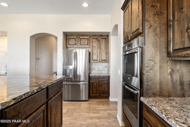 12300 W Slate Rd, Prescott, AZ 86305 - kitchen featuring light wood-style flooring, backsplash, dark stone counters, arched walkways, and appliances with stainless steel finishes