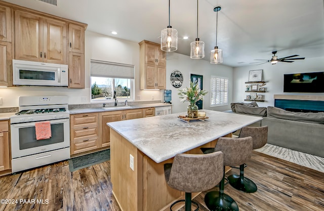 kitchen featuring hanging light fixtures, dark wood-type flooring, white appliances, a breakfast bar area, and a kitchen island