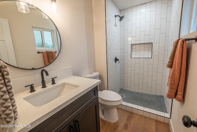 bathroom featuring toilet, wood finished floors, vanity, and a tile shower