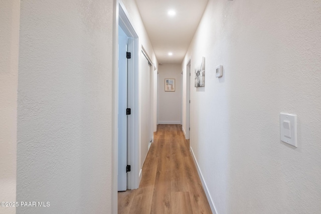 corridor with light wood-type flooring, baseboards, and a textured wall