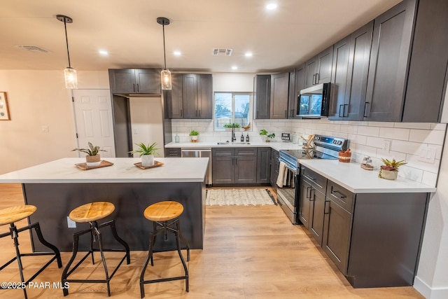 kitchen featuring visible vents, a kitchen bar, light wood-style floors, appliances with stainless steel finishes, and light countertops