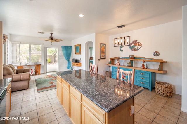 kitchen with dark stone counters, ceiling fan with notable chandelier, decorative light fixtures, a kitchen island, and light tile patterned flooring