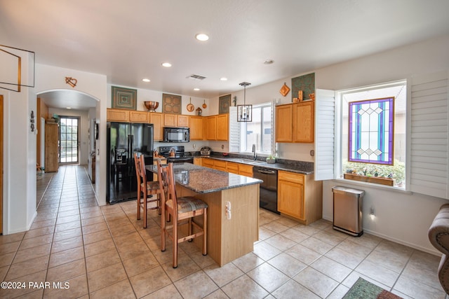 kitchen featuring light tile patterned floors, a center island, hanging light fixtures, and black appliances