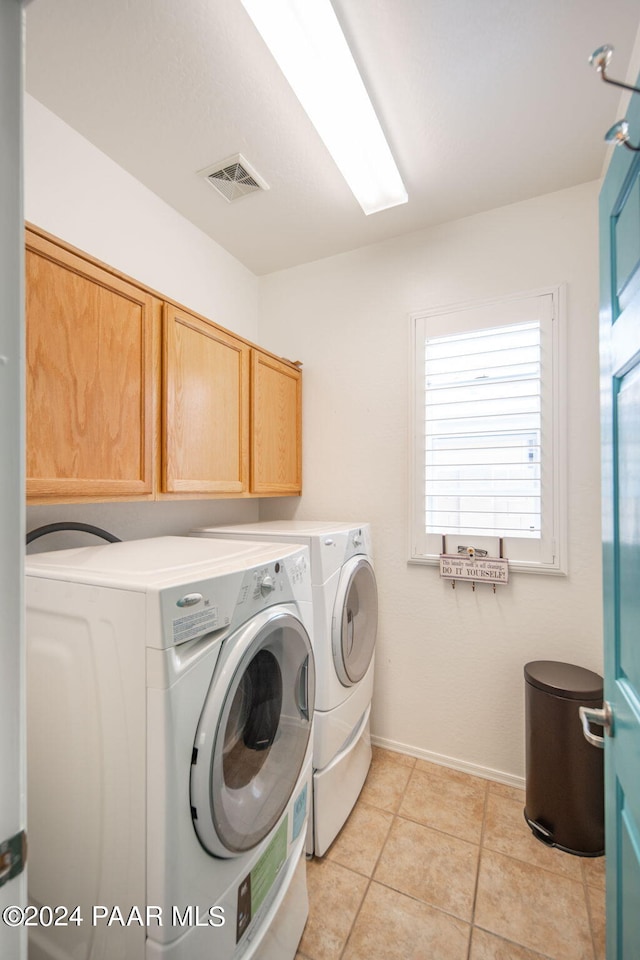 clothes washing area with cabinets, light tile patterned floors, and washer and clothes dryer