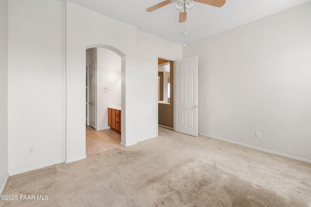 unfurnished bedroom featuring arched walkways, light carpet, baseboards, and ensuite bathroom