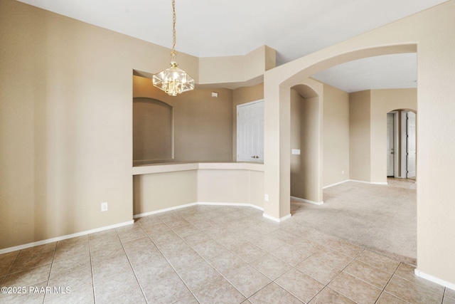 carpeted empty room with baseboards, arched walkways, and tile patterned flooring