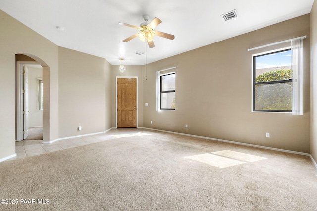 spare room featuring light tile patterned floors, visible vents, arched walkways, a ceiling fan, and light colored carpet