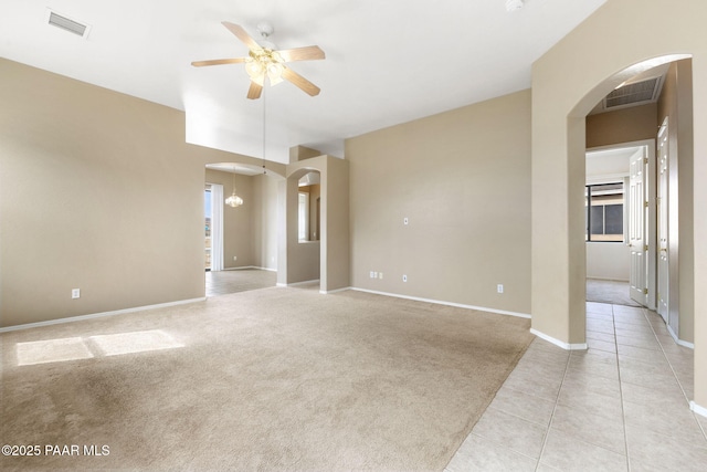 spare room featuring arched walkways, light tile patterned floors, visible vents, light carpet, and ceiling fan