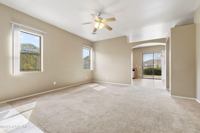 spare room featuring baseboards, visible vents, arched walkways, a ceiling fan, and light colored carpet