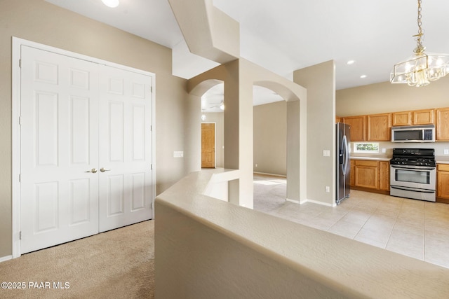 kitchen with arched walkways, light carpet, stainless steel appliances, hanging light fixtures, and light countertops