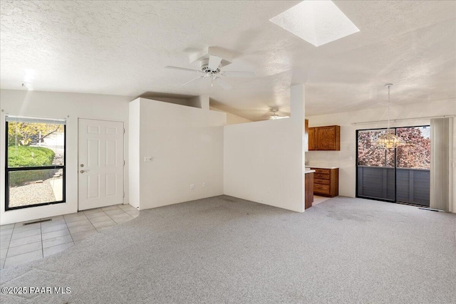unfurnished living room with ceiling fan with notable chandelier, a skylight, light carpet, and a textured ceiling