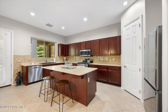 kitchen with sink, stainless steel appliances, light tile patterned floors, a breakfast bar area, and a kitchen island