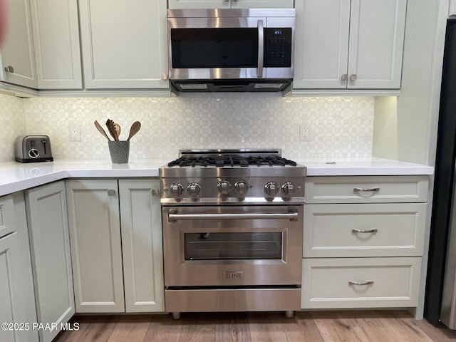 kitchen with tasteful backsplash, light wood finished floors, appliances with stainless steel finishes, and light countertops