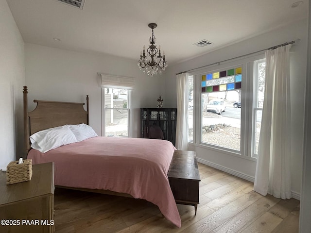 bedroom featuring light wood finished floors, visible vents, baseboards, and a notable chandelier