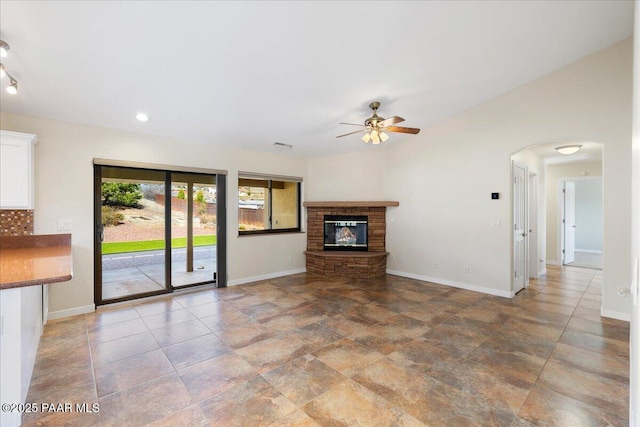 unfurnished living room with arched walkways, a fireplace, visible vents, ceiling fan, and baseboards