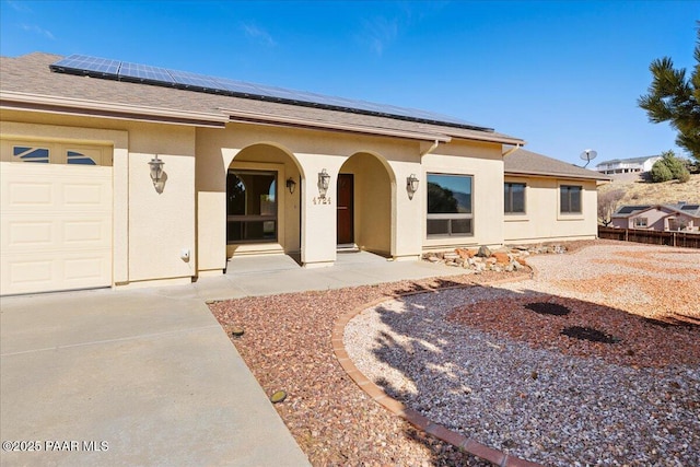 view of front facade featuring a shingled roof, solar panels, an attached garage, and stucco siding