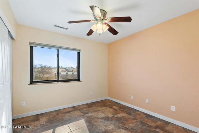 empty room featuring stone finish floor, baseboards, visible vents, and a ceiling fan