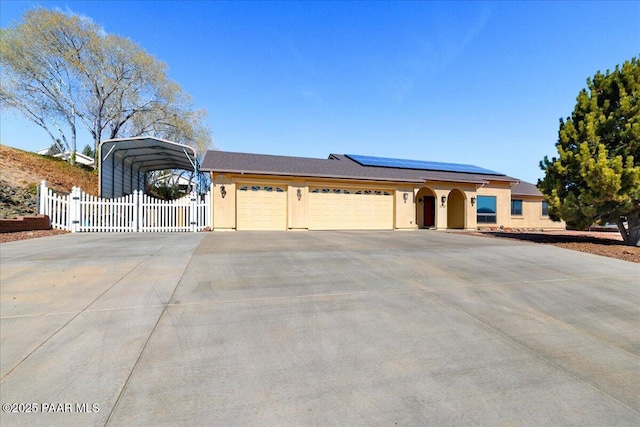 ranch-style home with concrete driveway, a gate, fence, roof mounted solar panels, and stucco siding