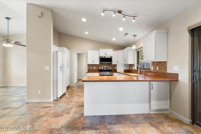 kitchen with appliances with stainless steel finishes, a peninsula, a sink, vaulted ceiling, and backsplash