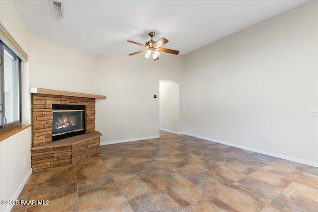 unfurnished living room featuring ceiling fan, a fireplace, arched walkways, and baseboards