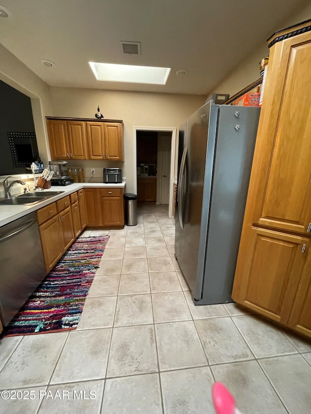 kitchen with a skylight, stainless steel appliances, light countertops, a sink, and light tile patterned flooring