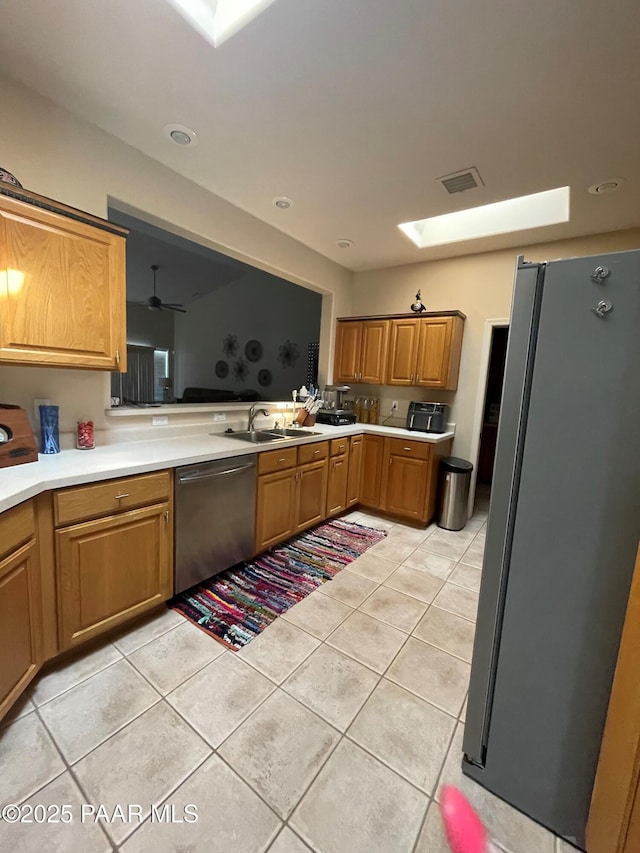 kitchen with a sink, light tile patterned floors, light countertops, a skylight, and appliances with stainless steel finishes