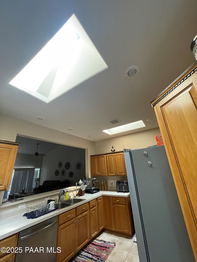 kitchen with a skylight, light tile patterned floors, appliances with stainless steel finishes, light countertops, and a sink