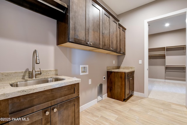 laundry room with hookup for a washing machine, cabinet space, electric dryer hookup, a sink, and light wood-type flooring